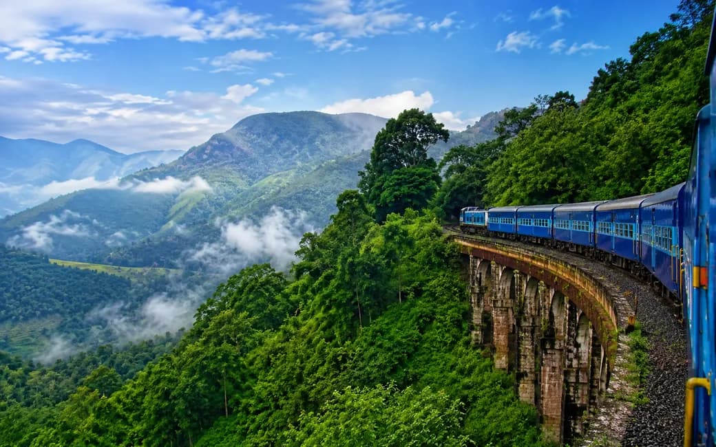 A train curving along a hillside viaduct through the forested Eastern Ghats